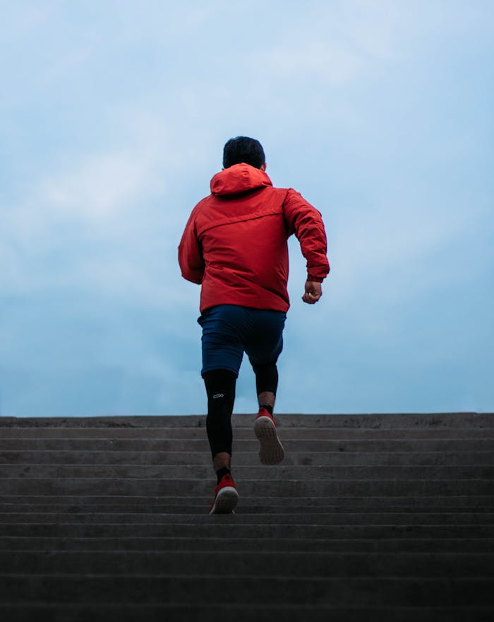 A man in a red jacket running up stairs outdoors, showcasing fitness and determination.